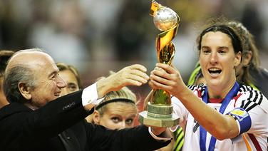 Die deutsche Nationalspielerin Birgit Prinz erhält den WM-Pokal von FIFA-Chef Sepp Blatter (Bild aus dem Jahr 2007) © imago/Ulmer 