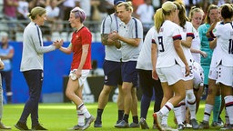US-Nationalspielerin Megan Rapinoe (M.) wird von Trainerin Jill Ellis (l.) auf dem Feld beglückwünscht. © imago images 