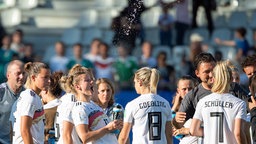 Die deutsche Fußball-Nationalspielerin Alexandra Popp (M.) steht mit mehreren anderen Spielerinnen auf dem Platz und spritzt Wasser aus einer Flasche. © dpa picture alliance Foto: Sebastian Gollnow