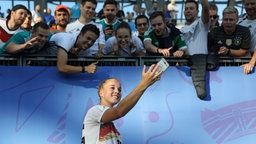 Die deutsche Fußball-Nationalspielerin Giulia Gwinn macht nach dem Spiel vor einer Tribüne im Stadion ein Selfie mit Fans. © dpa picture alliance/XinHua Foto: Xu Zijian