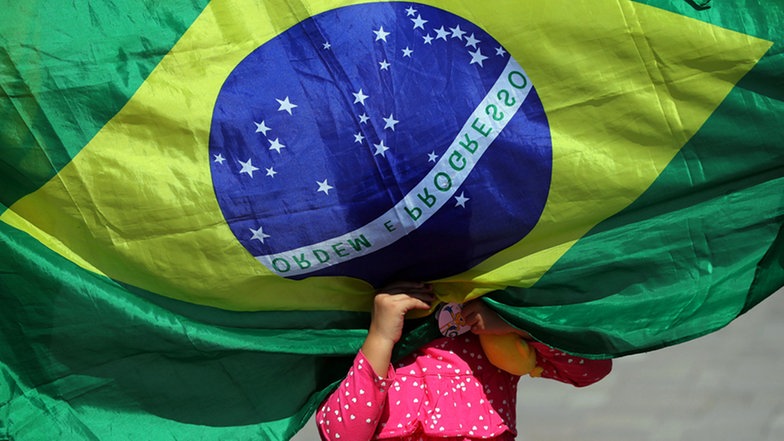 Eine brasilianisches Mädchen versteckt sich hinter der Brasilien-Flagge. © Imago/Agencia EFE