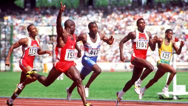 Ben Johnson jubelt über seinen 100-m-Sieg bei Olympia 1988. Später wird er wegen Dopings disqualifiziert. Carl Lewis (2.v.r.) erhält Gold. © picture-alliance / Sven Simon