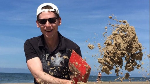 Frank Busemann mit Sonnenbrille und -hut beim Sandschaufeln  